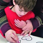 A young student receives help from a teacher in coloring a valentine.